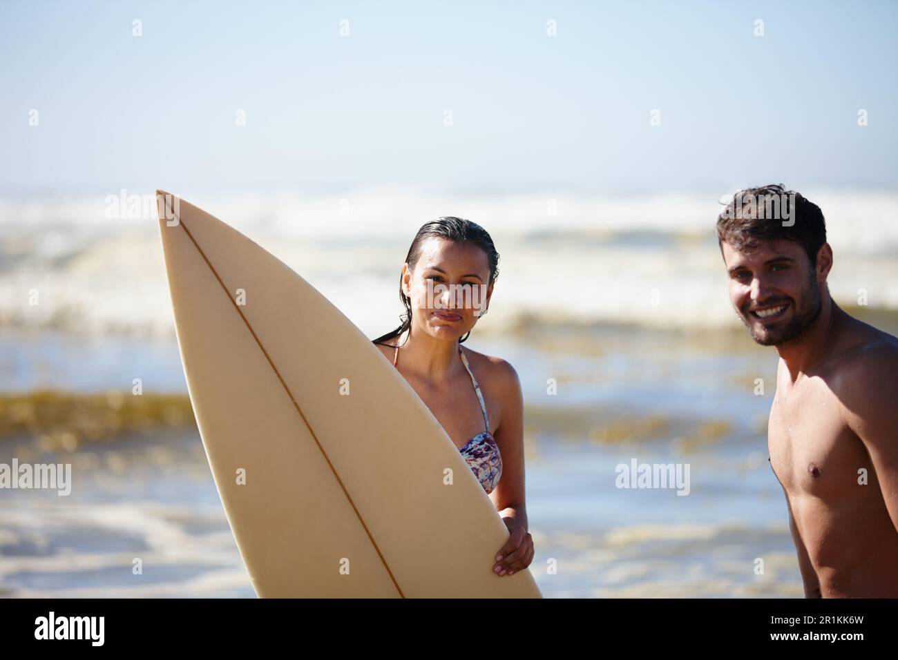 Unser Sommer. Porträtaufnahme eines glücklichen jungen Paares, das mit einem Surfbrett im Meer posiert. Stockfoto