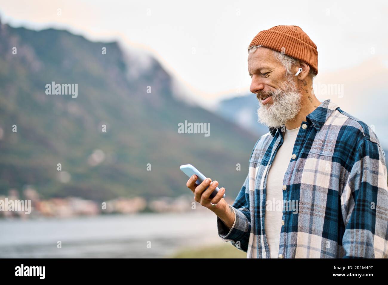 Älterer Hipster im Naturpark mit Ohrstöpseln am Telefon. Stockfoto