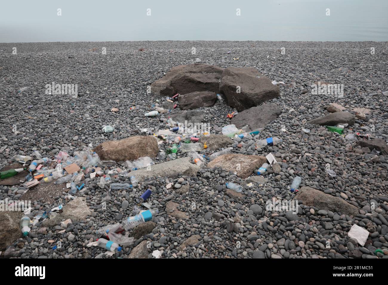 Müll verstreut auf Kieselsteinen nahe dem Meer. Recycling-Problem Stockfoto