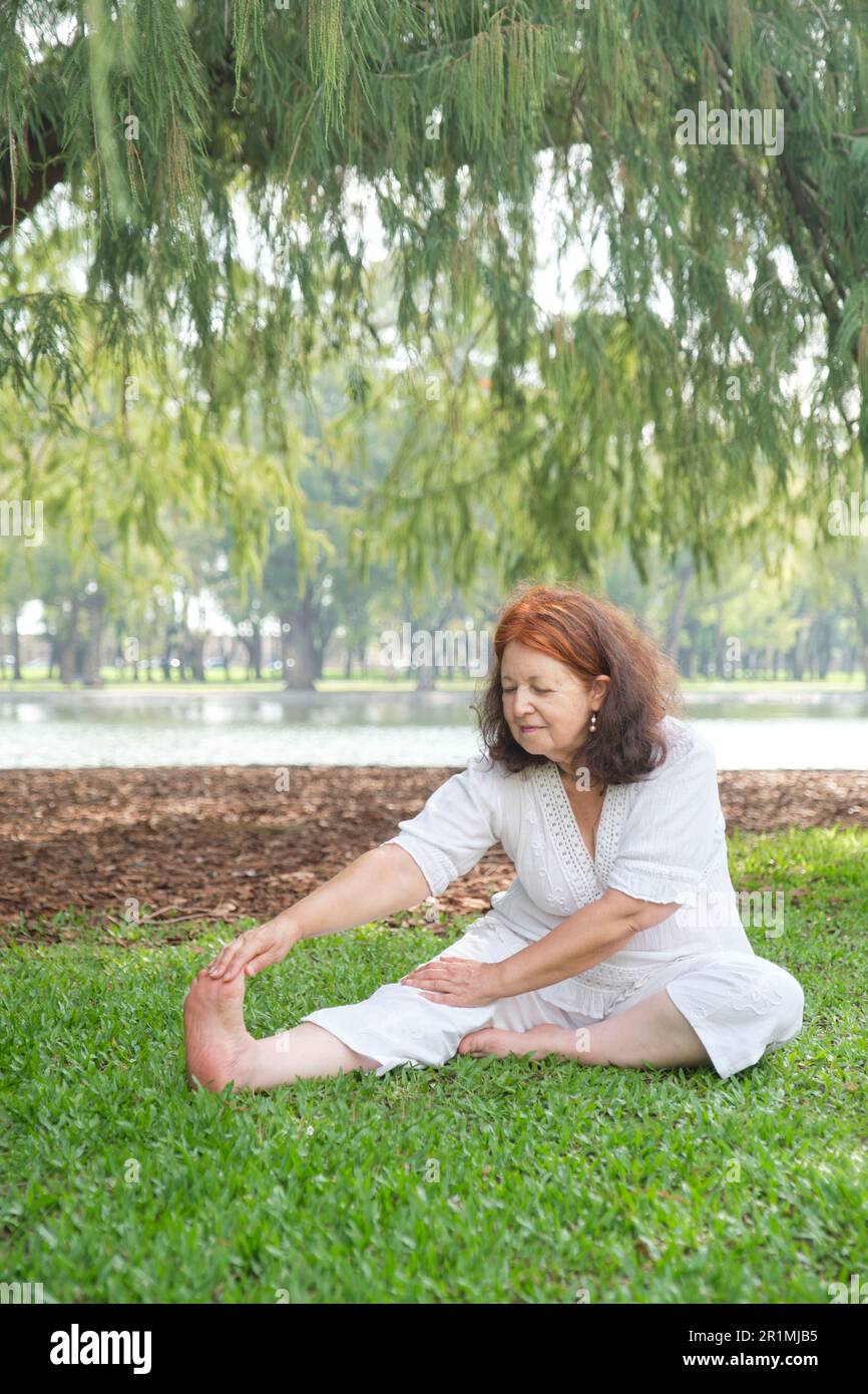 Reife lateinin in weißer Kleidung, die im Park Stretching-Übungen macht. Konzepte: Wellness, Vitalität, aktiver und gesunder Lebensstil. Stockfoto
