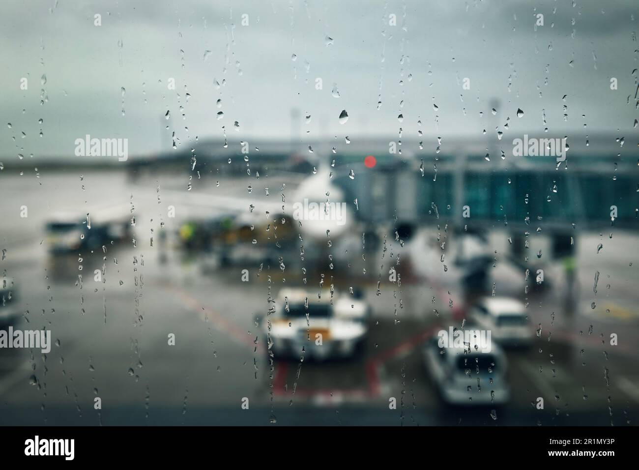 Düsteres Wetter am Flughafen. Selektiver Fokus auf Fallenlassen am Fenster des Terminals gegen Flugzeug im Regen. Stockfoto