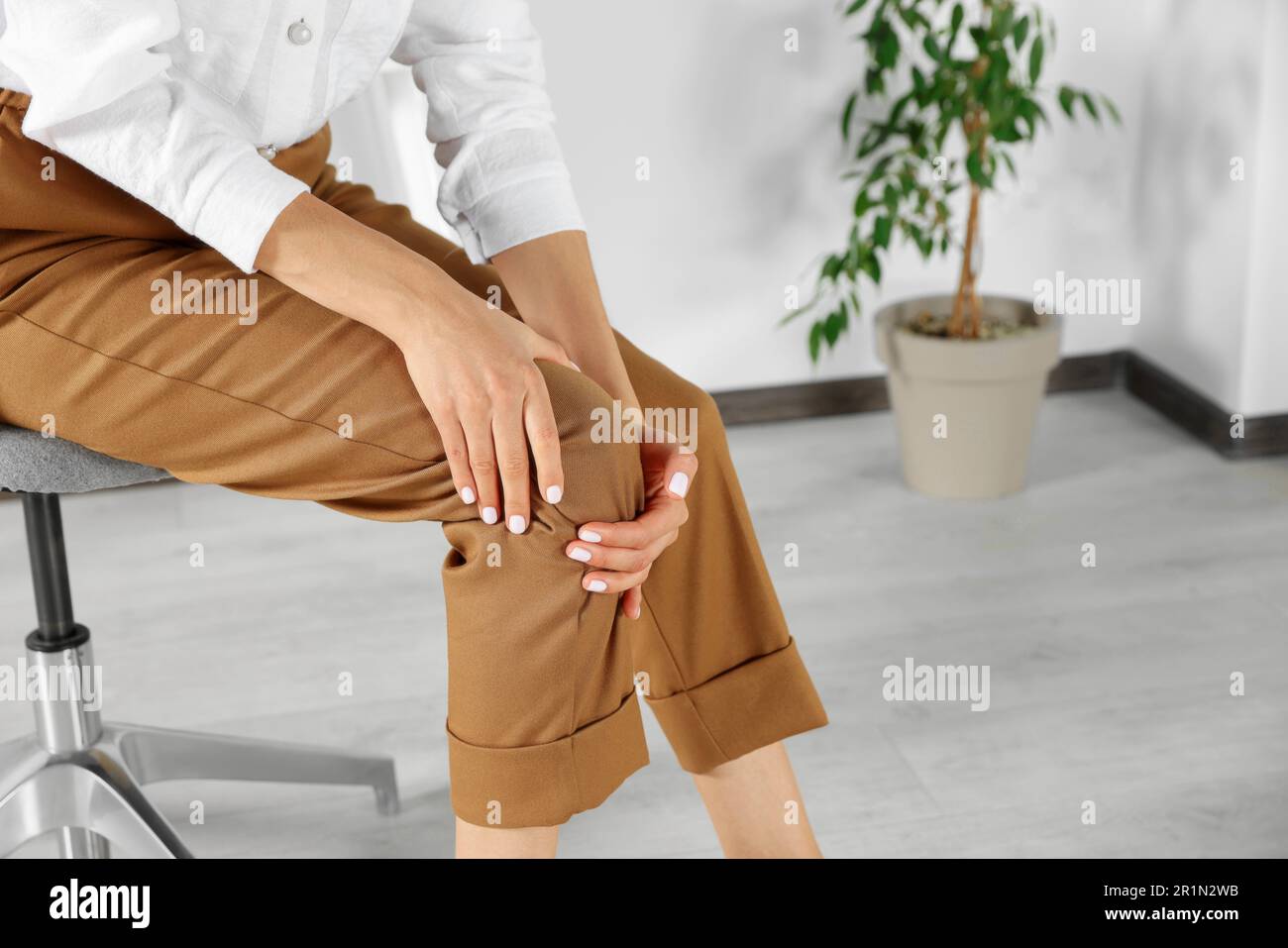 Eine Frau, die im Büro Kniescheiben reibt, Nahaufnahme. Platz für Text Stockfoto