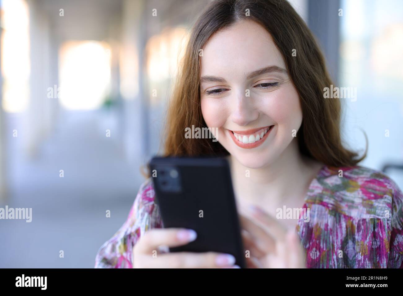 Glückliche Frau mit Smartphone, die auf einer Straße unterwegs ist Stockfoto