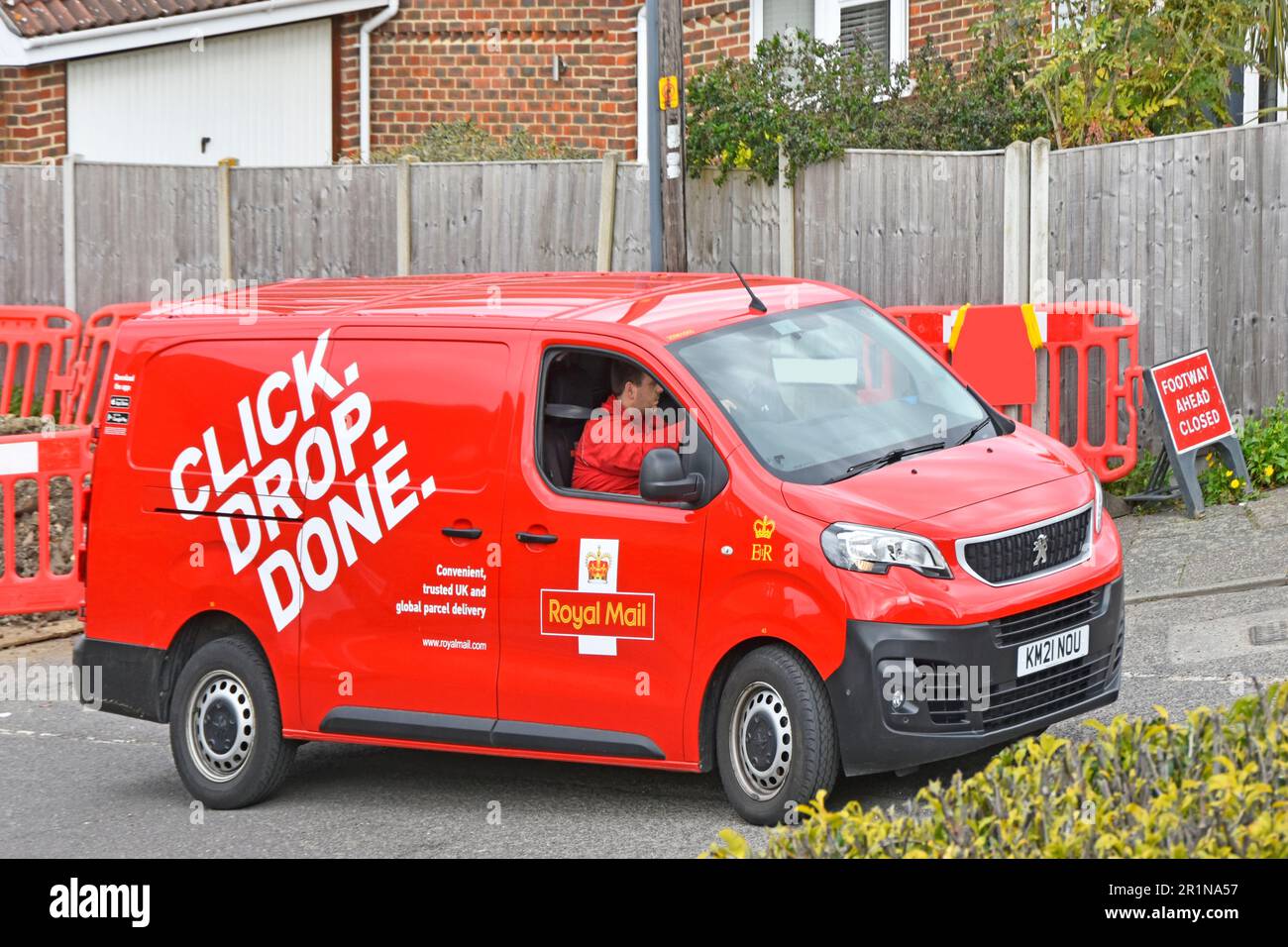 Klicken Sie auf den Slogan Drop Done auf der Seitenansicht des roten Royal Mail Postal Services Van-Fahrers, der sein Nutzfahrzeug bei Straßenarbeiten in Essex England UK manövriert Stockfoto