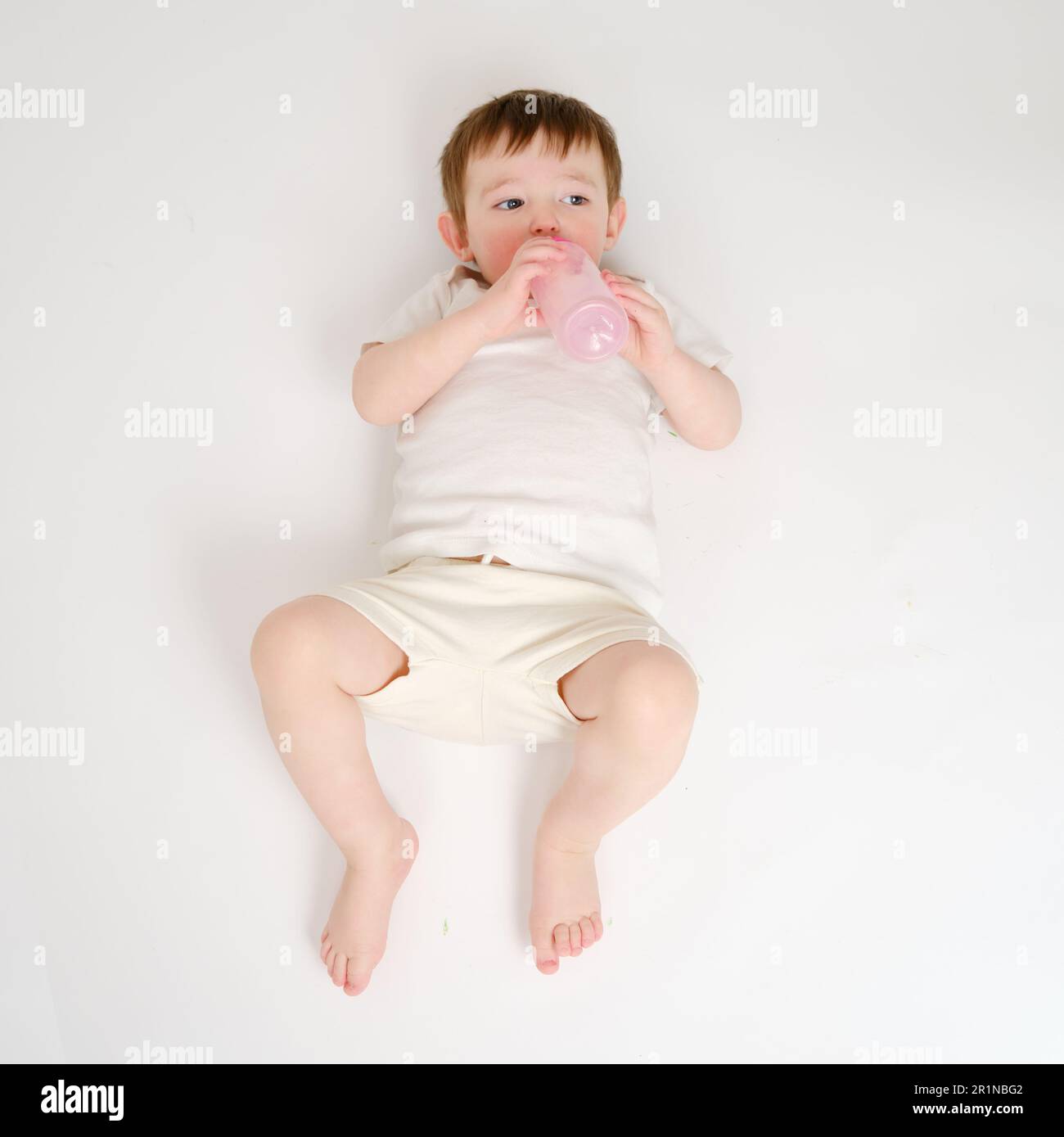 Happy Baby trinkt Milch aus der Flasche auf weißem Studiohintergrund. Ruhendes Kind isst Formel. Kind etwa zwei Jahre alt (ein Jahr neun Monate) Stockfoto