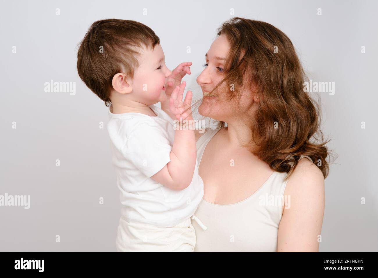 Glückliches Baby in den Armen einer Mutter auf weißem Studiohintergrund. Porträt eines 