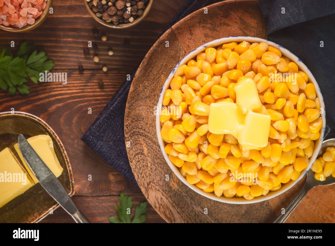 Zuckermaiskerne in einer kleinen Schüssel. Garniert mit köstlicher geschmolzener Butter. Serviert mit frischem Mais auf Maiskolben, Himalaya-Salz, Pfefferkörnern und Petersilie. Stockfoto