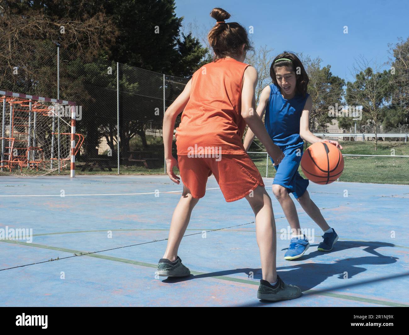 An einem sonnigen Frühlingstag stellen sich die Zwillingsbrüder bei einem Basketballspiel unter vier Augen auf einem Basketballfeld im Freien. Stockfoto