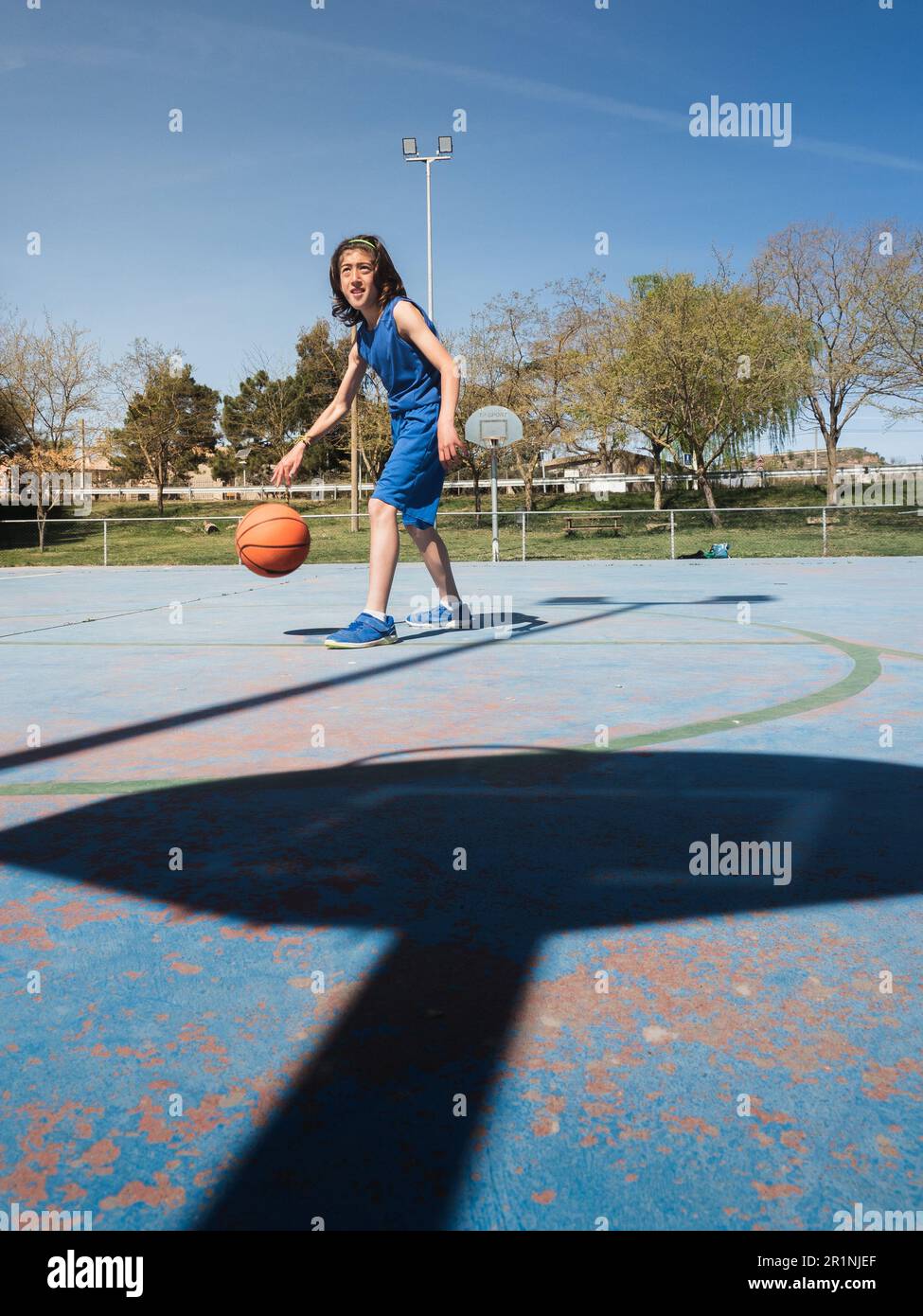 Junger Basketballspieler im Schatten des Korbs. Er hüpft den Ball über den Freiluftplatz. Stockfoto