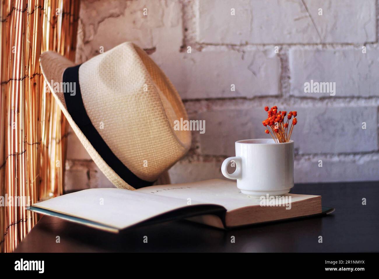 Ein Becher mit Blumen, ein Buch und ein Strohhut. Stockfoto