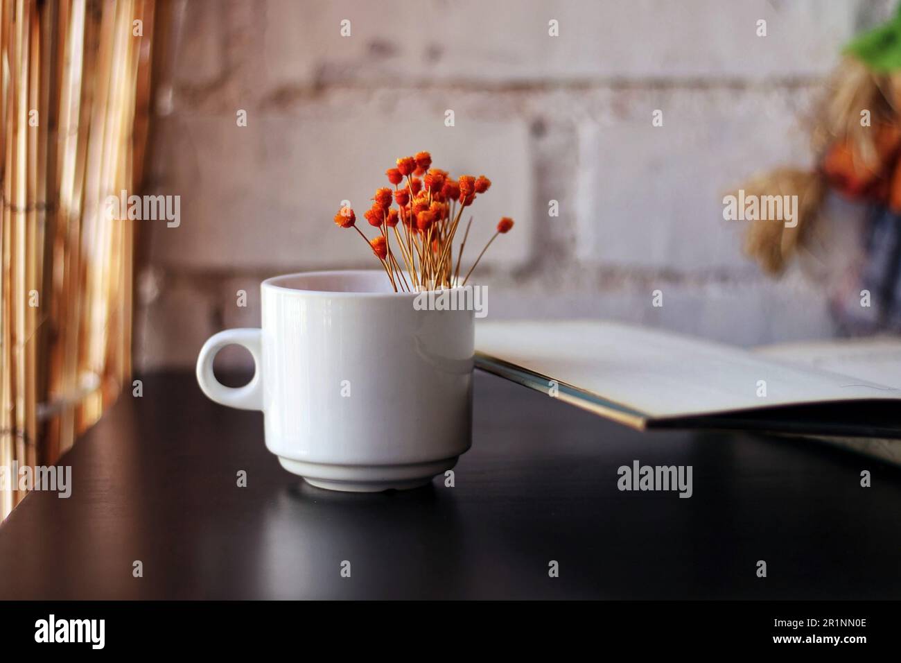 Das Buch ist neben einem Becher mit Blumen geöffnet. Stockfoto