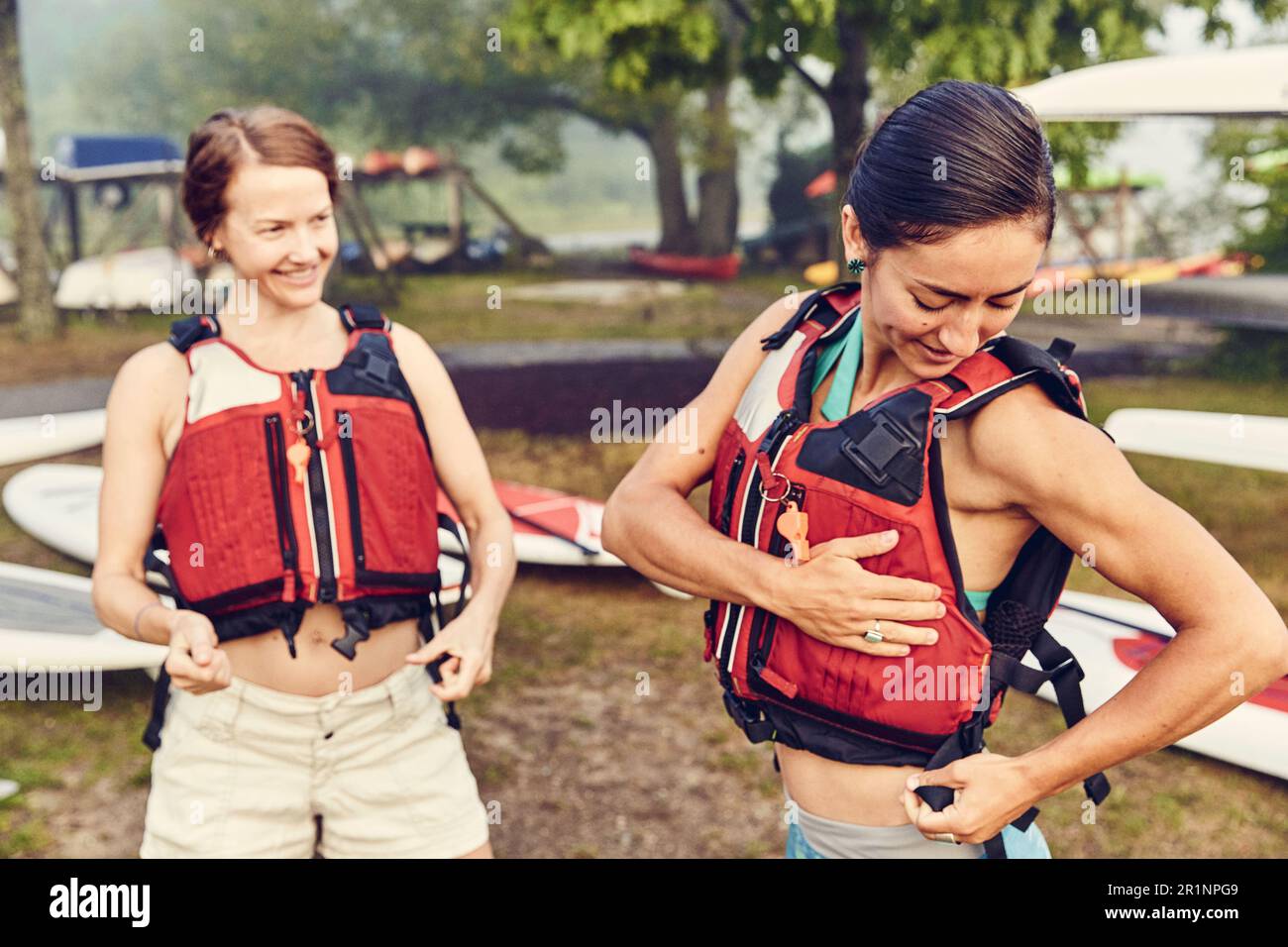 Junge Frauen ziehen ihre Schwimmwesten an, um sich auf den Kajakausflug vorzubereiten Stockfoto