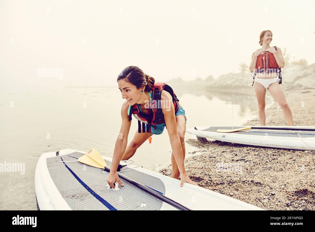 Junge Frauen lassen ihre Paddle-Boards an einem nebligen Morgen ins Wasser Stockfoto