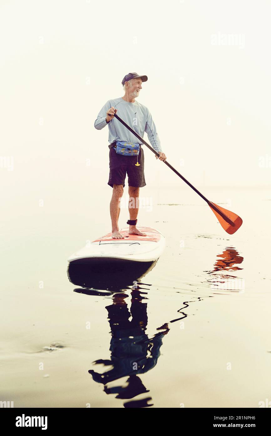 Ein erwachsener Mann, der an einem frühen nebligen Morgen steht und paddelt Stockfoto