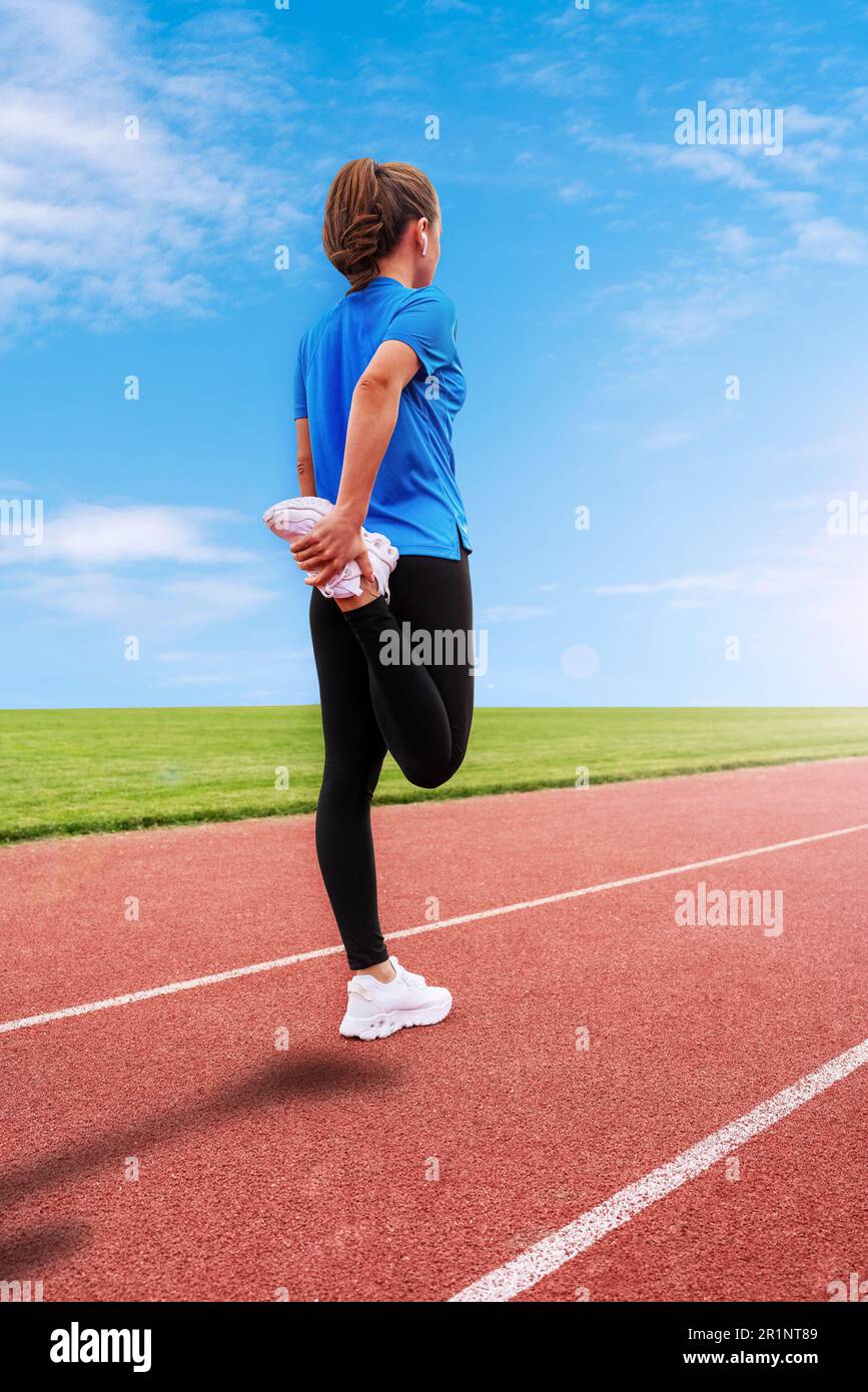 Sportlerin steht vor dem Start auf der Laufbahn und wärmt sich vor dem Lauf auf, reißt das Bein. Stockfoto