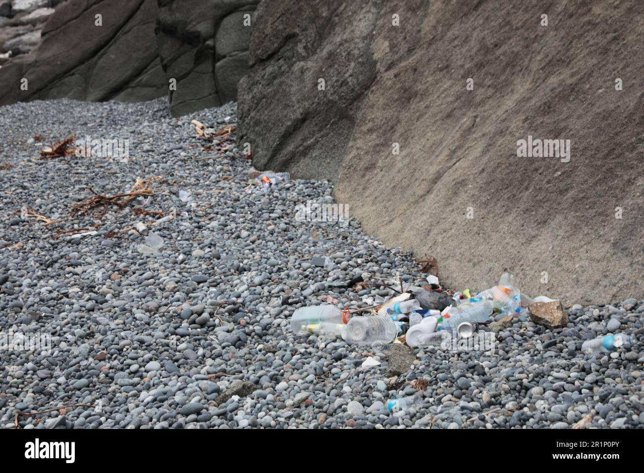 Müll verstreut auf Kieseln in der Nähe von Felsen. Recycling-Problem Stockfoto