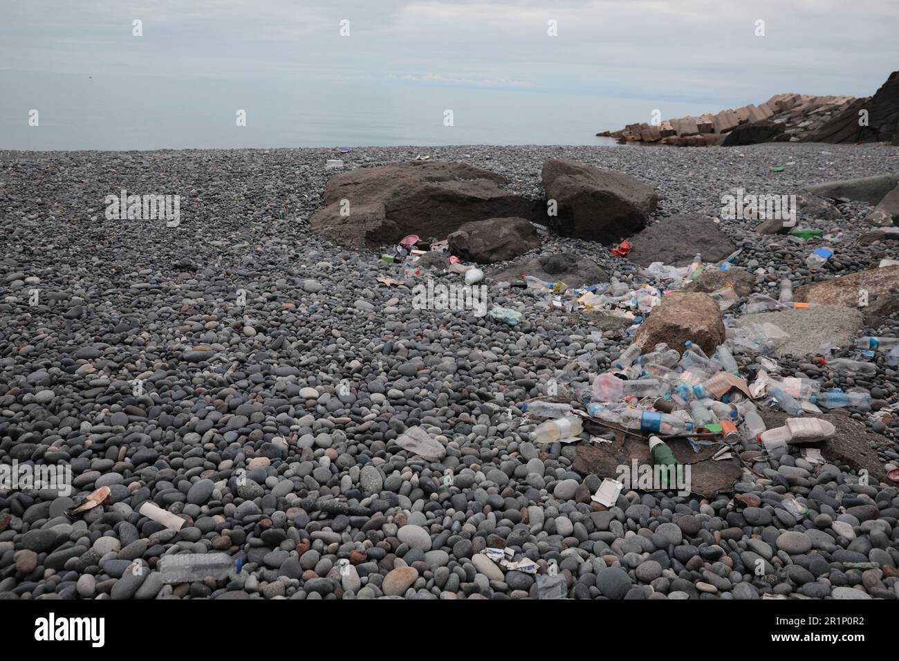 Müll verstreut auf Kieselsteinen nahe dem Meer. Recycling-Problem Stockfoto