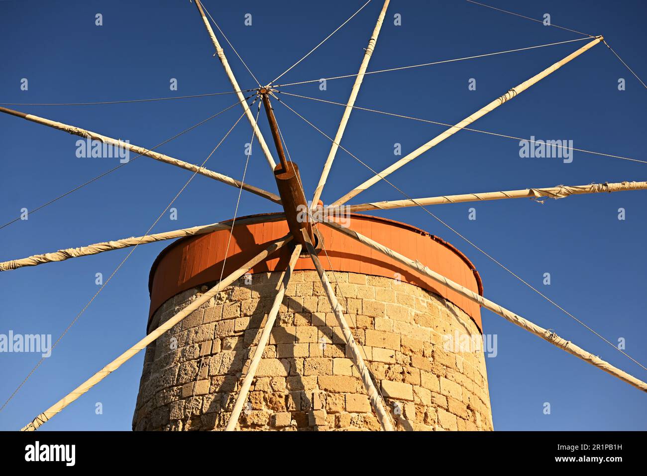 Ein halbrunder Steinturm mit einem roten konischen Dach. Mittelalterliche Mühle mit Holzwindmühlen vor dem blauen Himmel. Nahaufnahme des Turms. Stockfoto