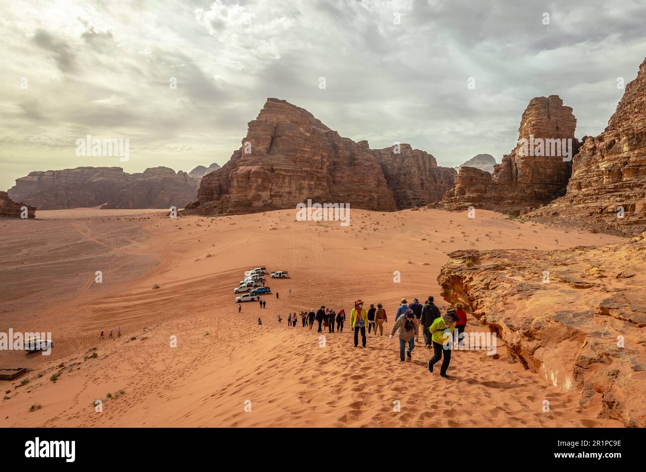 Touristen, die eine Sanddüne unter dem dramatischen Himmel erklimmen. Wadi Rum, Jordanien. Stockfoto