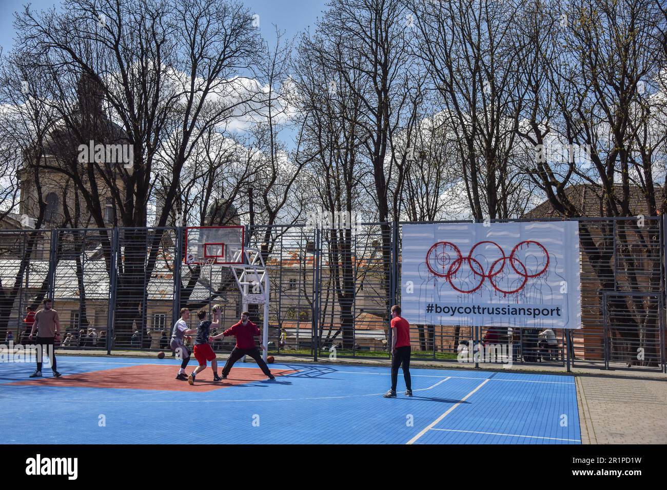Die Leute spielen Basketball auf einem Banner mit der Inschrift #BoycottRussianSport auf einem der Sportplätze in Lemberg. Die Ukraine und viele Länder auf der ganzen Welt fordern, dass russische Athleten wegen des von Russland ausgelösten russisch-ukrainischen Krieges von den Olympischen Spielen und anderen internationalen Wettkämpfen ausgeschlossen werden. Viele ukrainische Athleten, die die Ukraine vor dem russischen Aggressor verteidigten, sind bereits in diesem Krieg gestorben. Zur Unterstützung des Boykotts wurde ein Banner mit der Aufschrift #BoycottRussianSport auf einem der Sportplätze in Lemberg aufgehängt. Stockfoto
