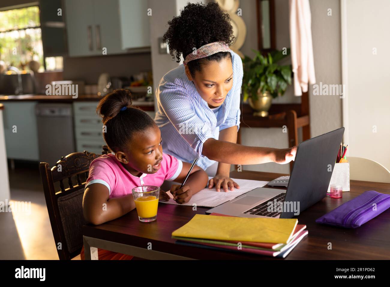 afroamerikanische Mutter hilft ihrer glücklichen Tochter, die zu Hause mit einem Laptop Schularbeiten macht Stockfoto