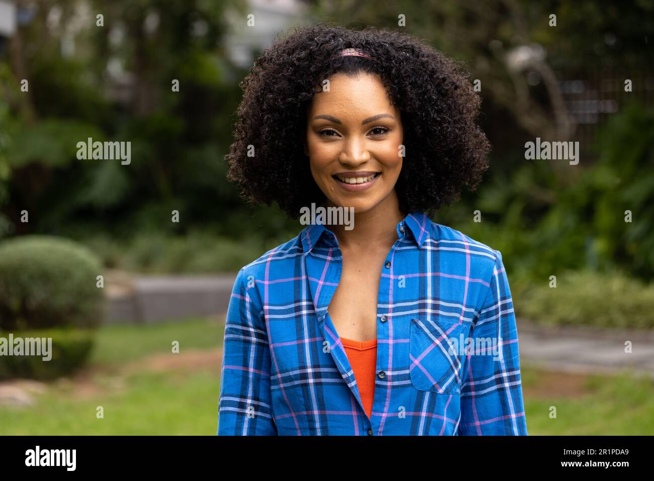 Porträt einer glücklichen afroamerikanischen Frau, die ein kariertes Hemd trägt und im Garten lächelt Stockfoto