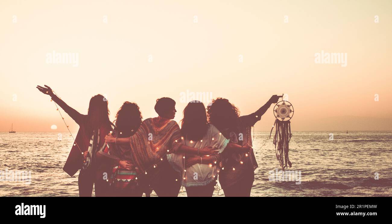 Traumhafte Tagträumer-Menschen-Konzept mit einer Gruppe weiblicher Freundinnen, die den goldenen Sonnenuntergang am Strand mit Blick auf das Meer genießen und einen Traumfänger halten. Das Konzept glücklicher Reiselebensleute Stockfoto