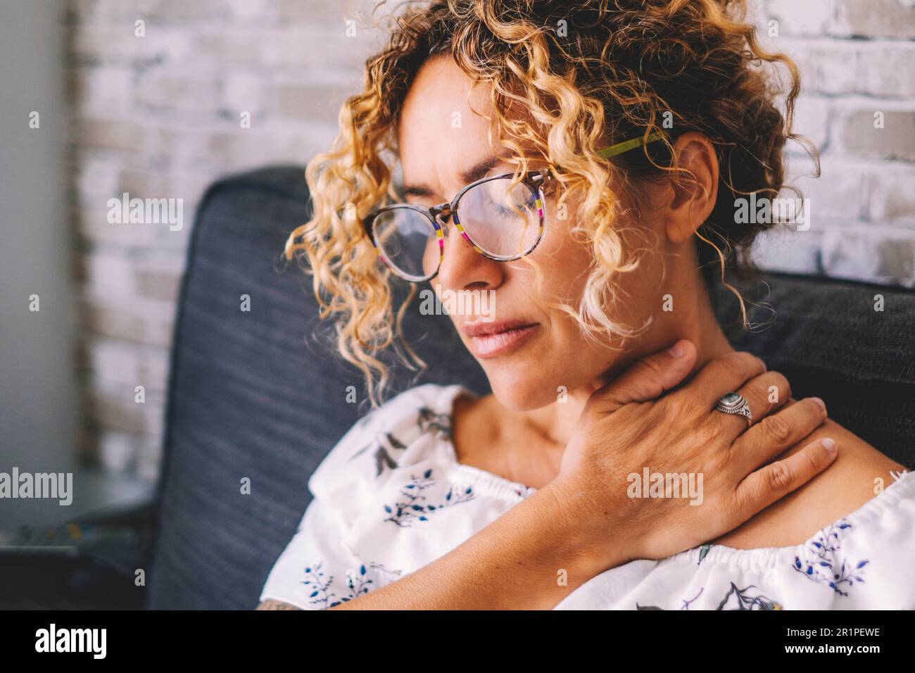 Kranke Erwachsene im mittleren Alter junge Frauen, die den Hals berühren, leiden unter Schulter- und Nackenschmerzen. Weibliche Schulterkranke zu Hause auf dem Sofa sitzen Stockfoto