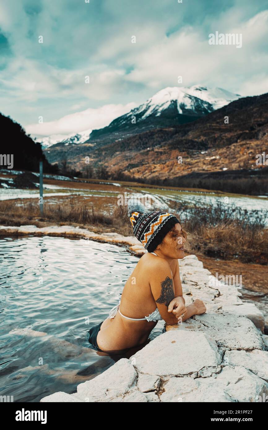 Eine Touristin genießt im Winter ein heißes Thermalwasser, ein natürliches Spa für Wellness und neue Outdoor-Erlebnisse mit Blick auf die Schneeräume. Weibliche Freizeitaktivitäten im Naturpool und Reiseziel Stockfoto