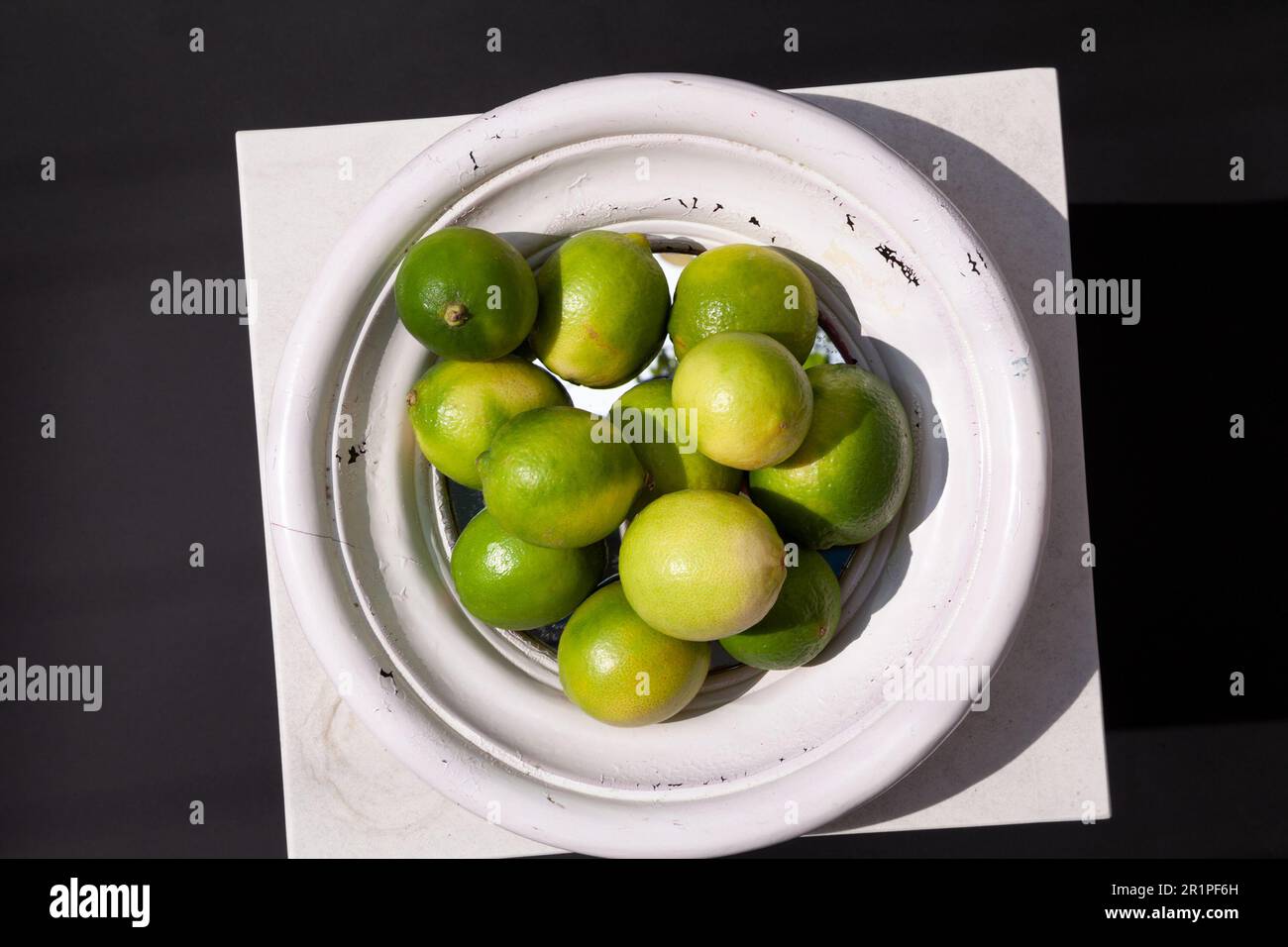Eine Obstschale voller grüner Limetten auf einem weißen Tisch als dekoratives Innenelement. Abstraktes künstlerisches Stillleben mit geometrischen Elementen, Licht Stockfoto