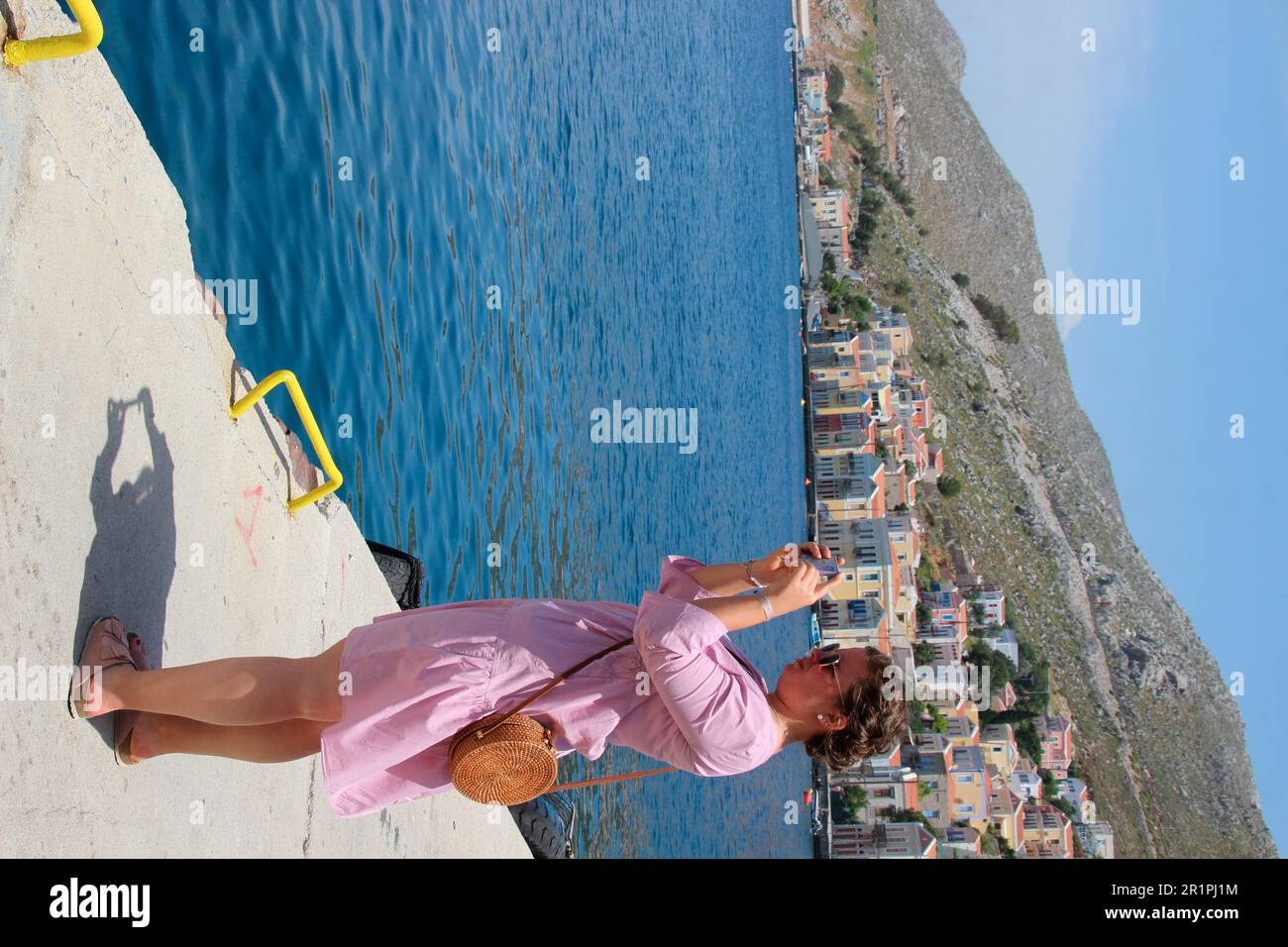 Junge Frau macht Handyfoto auf der Hafenpromenade von Simy, Griechenland, Stockfoto