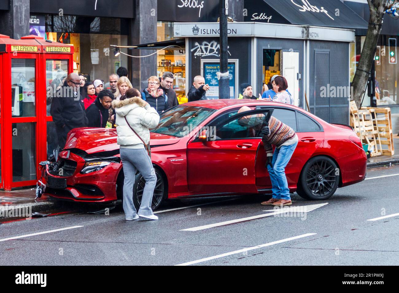 Zuschauer drängen sich um einen roten Mercedes, der in der Holloway Road, North London, Großbritannien, gerutscht und abgestürzt ist Stockfoto