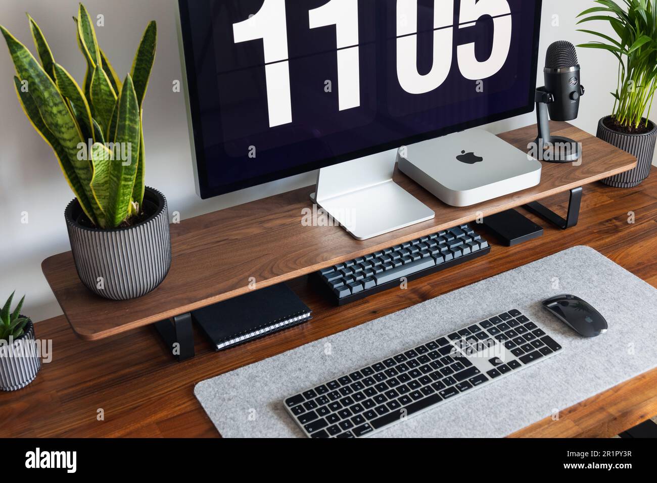LONDON – 15. MAI 2023: Minimaler Schreibtischeinsatz in einem modernen Heimbüro mit Pflanzen, Walnussholz, Apple Mac Mini-Computer mit Logo Stockfoto