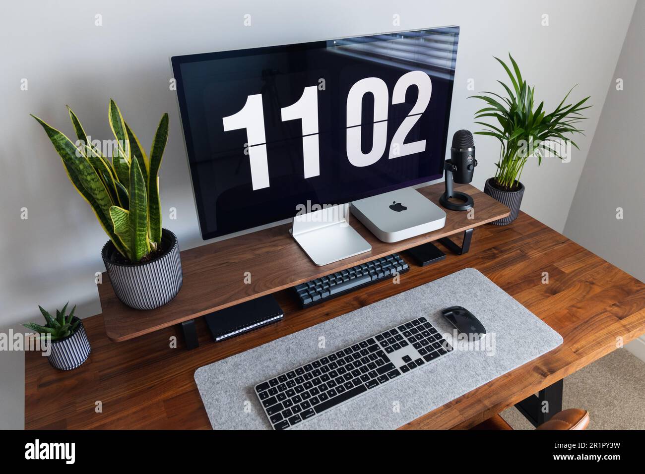 LONDON – 15. MAI 2023: Minimaler Schreibtischeinsatz in einem modernen Heimbüro mit Pflanzen, Walnussholz, Apple Mac Mini-Computer mit Logo Stockfoto