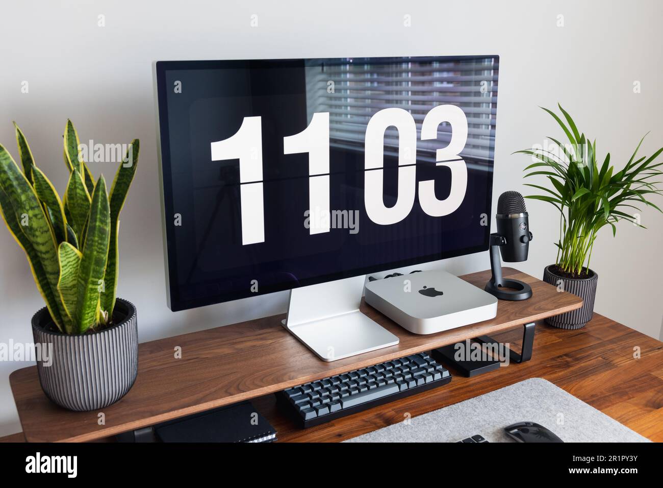 LONDON – 15. MAI 2023: Minimaler Schreibtischeinsatz in einem modernen Heimbüro mit Pflanzen, Walnussholz, Apple Mac Mini-Computer mit Logo Stockfoto