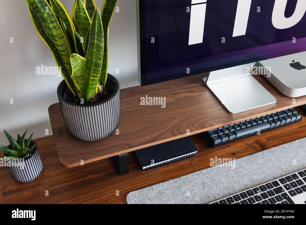 LONDON – 15. MAI 2023: Minimaler Schreibtischeinsatz in einem modernen Heimbüro mit Pflanzen, Walnussholz, Apple Mac Mini-Computer mit Logo Stockfoto