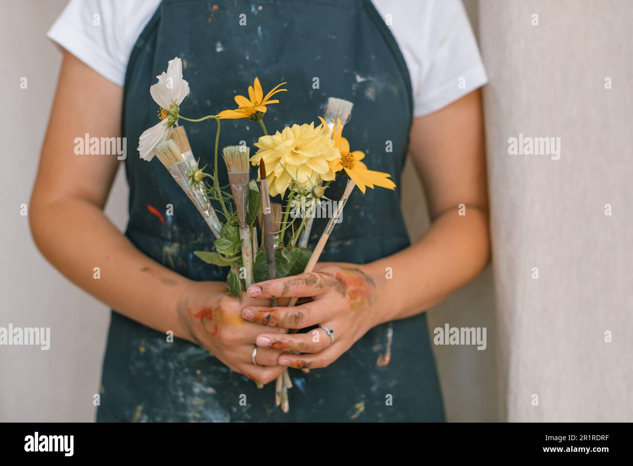 Nahaufnahme eines jungen Künstlers mit einem Blumenstrauß aus Blumen und Pinseln im Studio Stockfoto