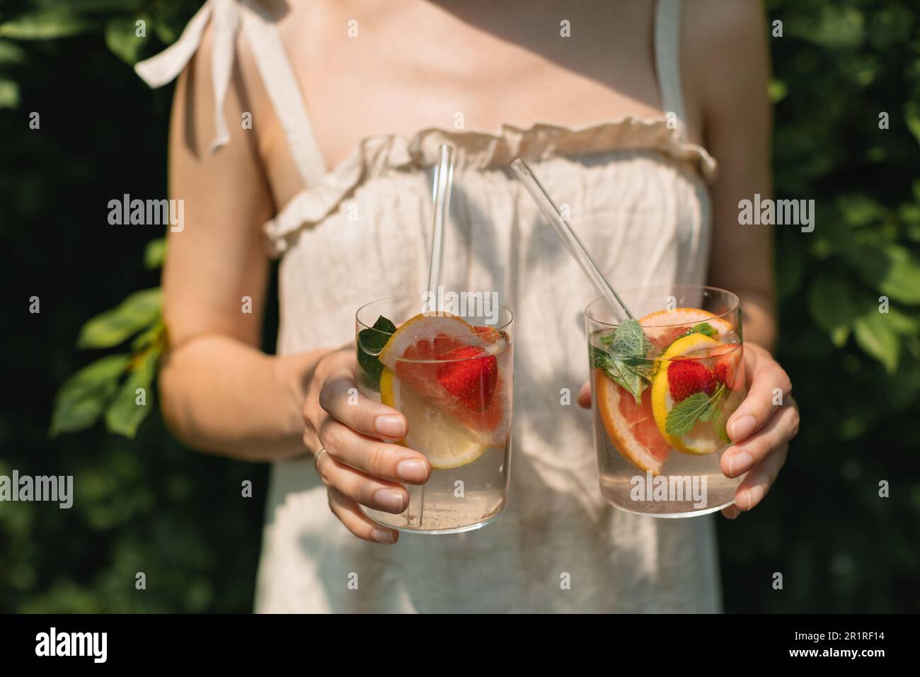 Nahaufnahme einer Frau in einem Sommerkleid mit zwei Fruchtgetränken Stockfoto