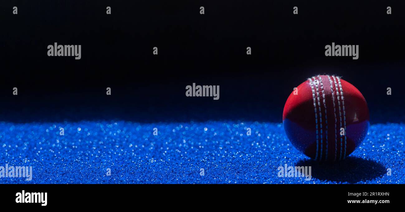 Cricket-roter Ball mit natürlichem Licht auf blauem Hintergrund. Horizontales Sportposter, Grußkarten, Kopfzeilen, Website und App Stockfoto