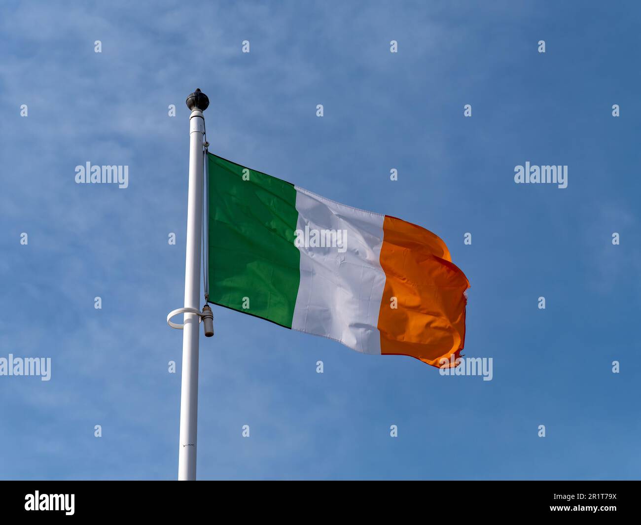 Eine irische Flagge auf einem Flaggenmast vor einem klaren blauen Himmel. Stockfoto