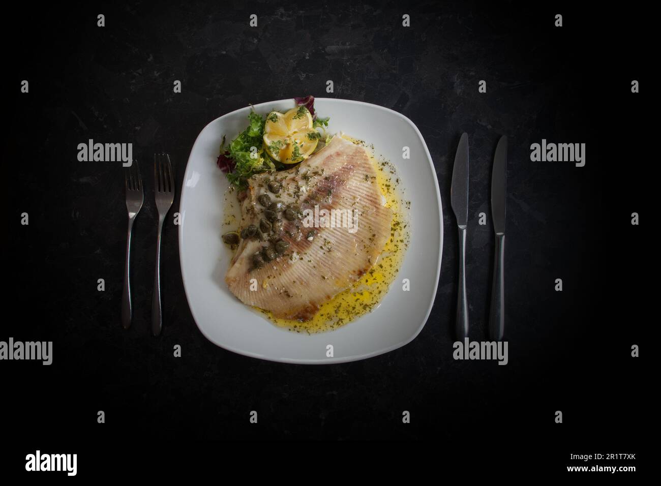 Gekochter Schlittschuh mit Buttersauce, Kapern und Zitrone auf einem weißen Teller. Flach, schwarzer Hintergrund. Stockfoto