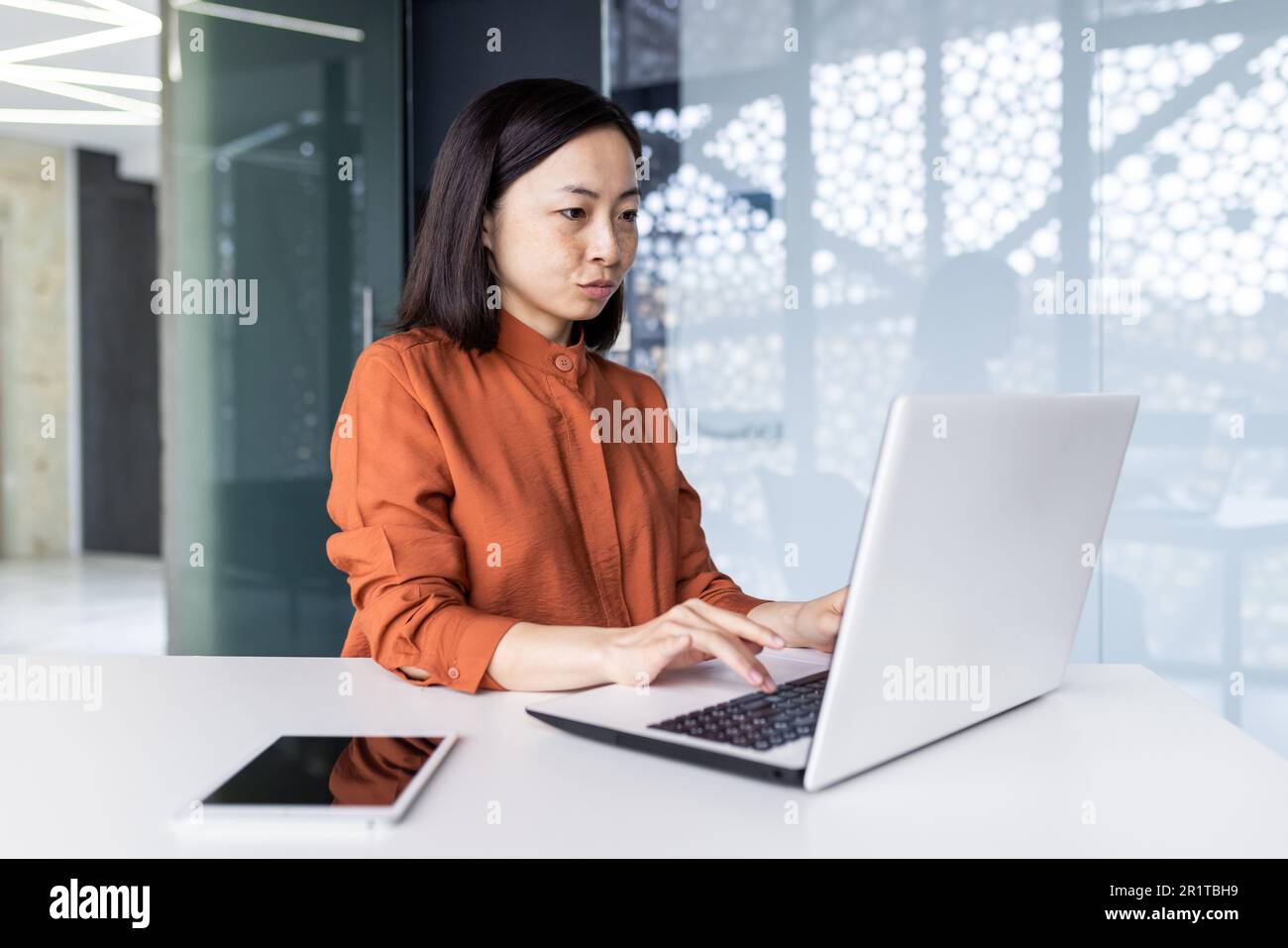 Junge asiatische Programmiererin, Entwicklerin und Tester sind fokussiert und arbeiten ernsthaft im Büro an einem Laptop. Stockfoto