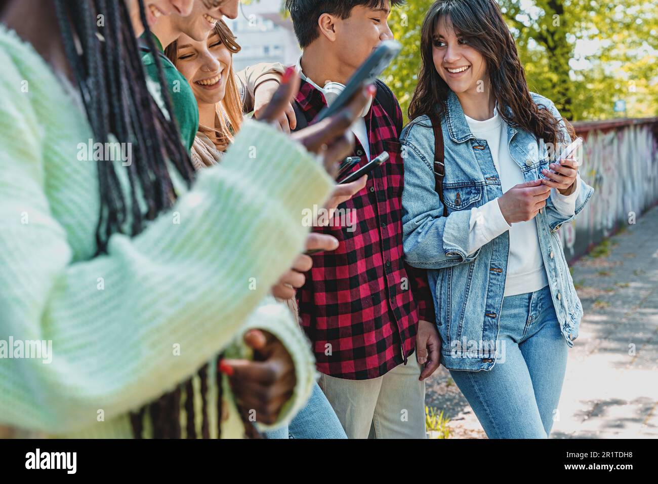 Eine vielfältige Gruppe von Studenten der Generation Z versammelte sich in einem Park. Die jungen Leute machen Scherze und überprüfen soziale Netzwerke auf ihren Smartphones. Stockfoto