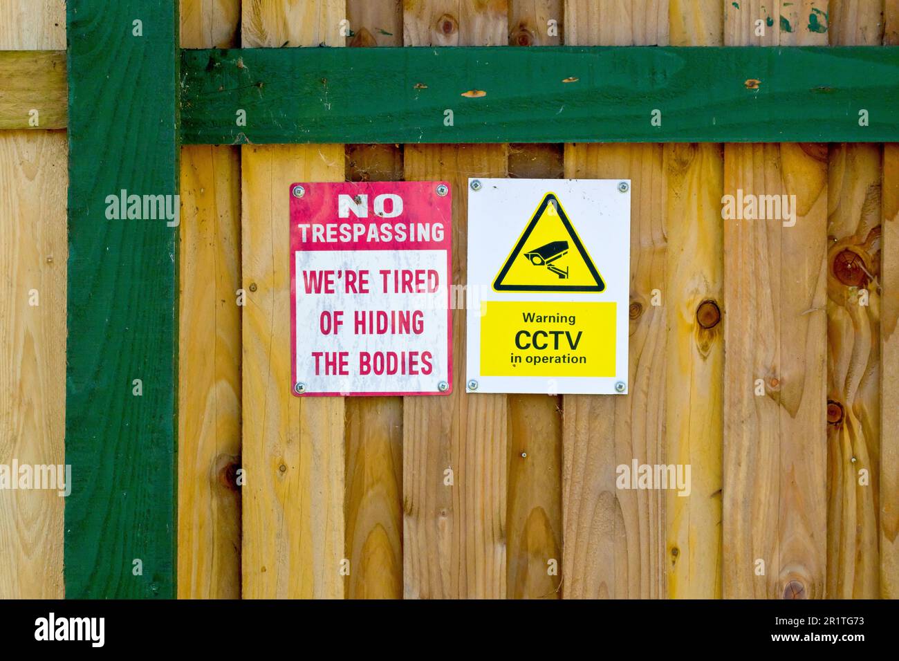 Nahaufnahme von zwei Warnschildern, die am Zaun eines abgelegenen Hauses angebracht sind, ein General für Videoüberwachung, das andere leichtherzig und humorvoll. Stockfoto