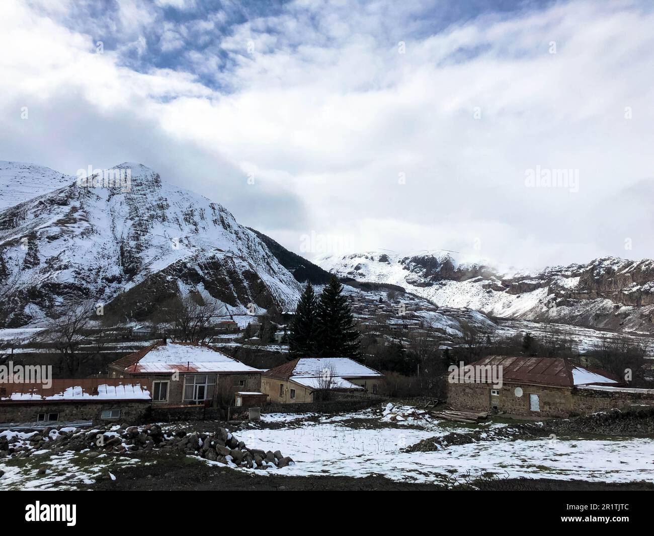 Kleine Steinhäuser, Gebäude im Dorf in einem wunderschönen bergigen kalten Winterresort mit hohen Berggipfeln, Nebel und schneebedeckten Felsen für Schneefall Stockfoto