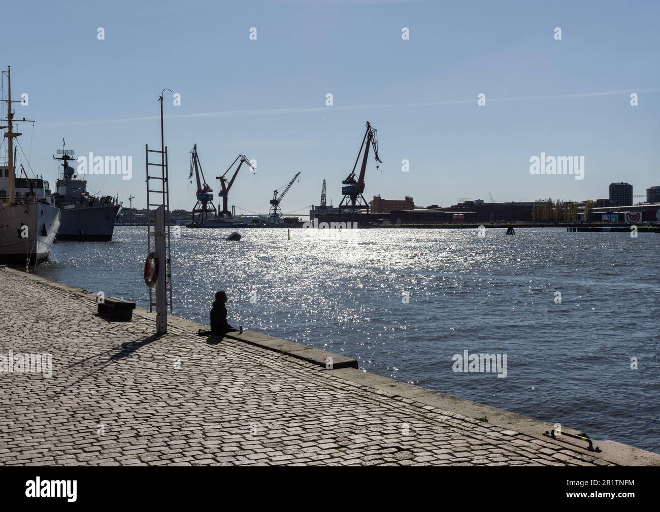 Silhouette einer Person mit Blick auf den Gota-Kanal, Gota Alv mit Kränen und Schiffen im Hintergrund von Jussi Bjorling Plats. Göteborg Stockfoto