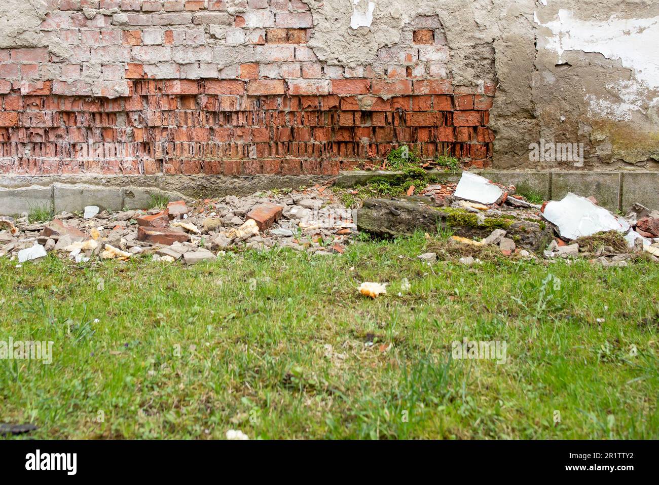 Einstürzende Wand aufgrund von Wassereintritt, verschlissene rote Ziegelwand und grünes Gras Stockfoto