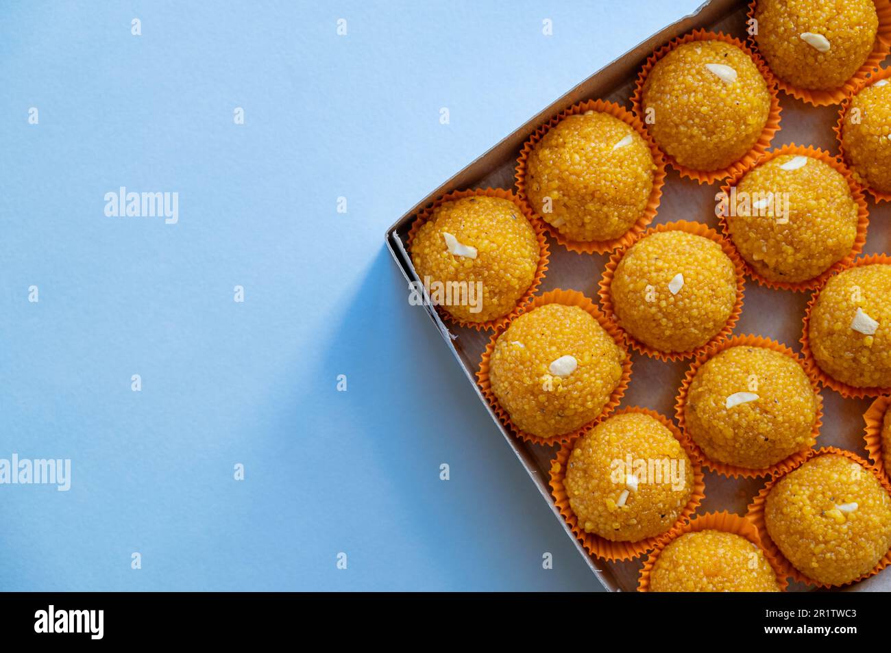 Laddu Sweets in der Verpackung mit hellblauem Hintergrund und Kopierraum. Laddu oder Laddoo ist kugelförmiger indischer Süßstoff aus verschiedenen Zutaten. Stockfoto