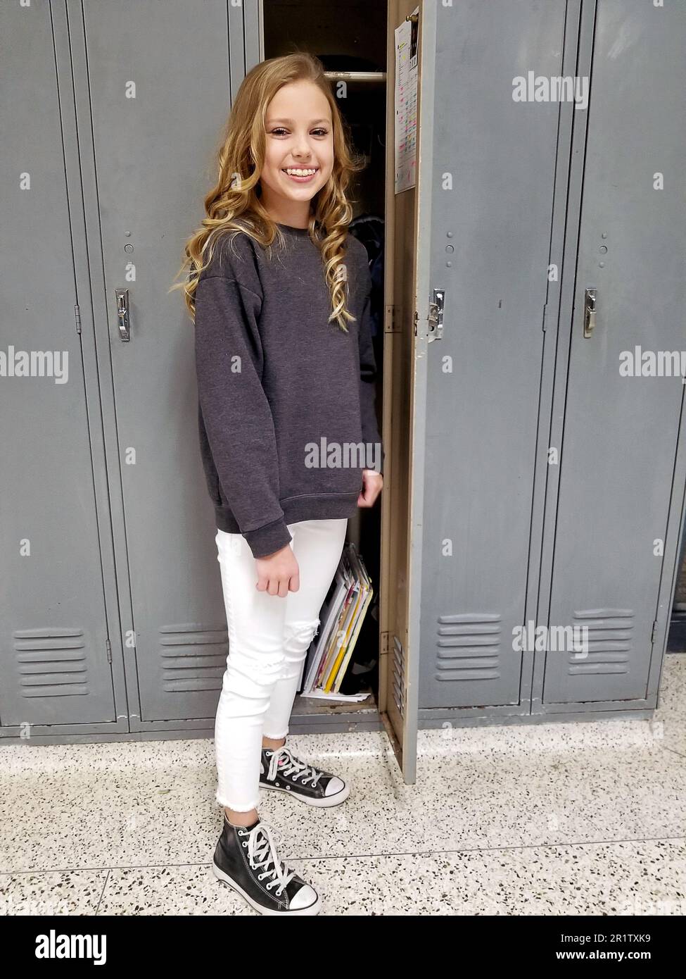 Blondes, weißes Mädchen steht in grauen Schließfächern im Schulflur Stockfoto