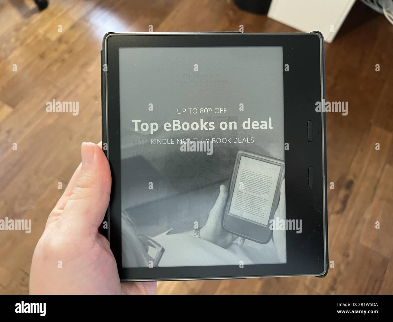 Vereinigte Staaten. 07. November 2022. Ein wenig aus einem hohen Winkel gezogenes Bild einer Hand mit einem Kindle eReader, der mit „80 % Rabatt auf Top eBooks“ und einem Holzboden im Hintergrund wirbt, Lafayette, Kalifornien, 7. November 2022. Foto mit freundlicher Genehmigung von Sftm. (Foto: Gado/Sipa USA) Guthaben: SIPA USA/Alamy Live News Stockfoto